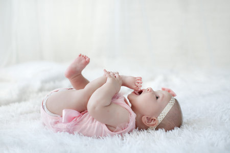 Cute adorable baby girl flying alone dressed on a white bed.Little child looking at the camera. Baby...