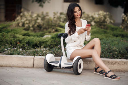Beautiful girl in white summer dressing up in the summer outdoors . Good weather trendy transportation technologyの写真素材