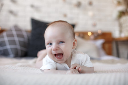 Adorable baby boy in white sunny bedroom in winter morning. Newborn child relaxing in bed. Family...