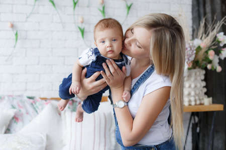 Young mother holding her newborn child. Woman and new born boy relax in a white bedroom. A young mother gently holds her newborn son in her arms. Family at home. Young mother playing whith her newborn sonの写真素材