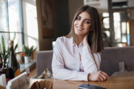 Beautiful woman at a table in a cafe. Young woman sitting at a table in a cafe. Tanned skin casual makeup. Waiting for lunch in a restaurant.の写真素材