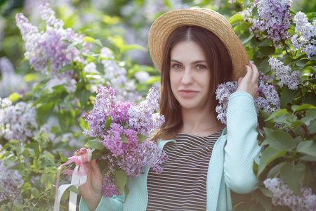 Young beautiful woman enjoying the smell of blooming lilac on a sunny day. Summer girl in the parkの写真素材