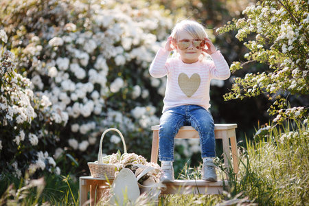 A girl is sitting in the spring park, sitting against a background of white flowering bushes. Spring...