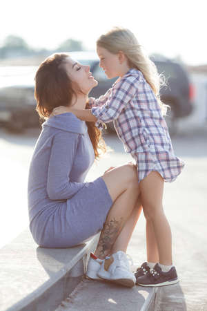Mother and daughter outdoors in city. playing and having fun. Happy little girl and baby daughter in bright sunlight. Beautiful portrait. Real emotions.の写真素材