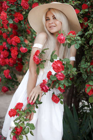 Perfume and cosmetics. Woman in front of blooming roses bush. Blossom of wild roses. Aroma of roses. Girl adorable blonde sniffing fragrance of pink bloom. Outdoors in the spring gardenの写真素材
