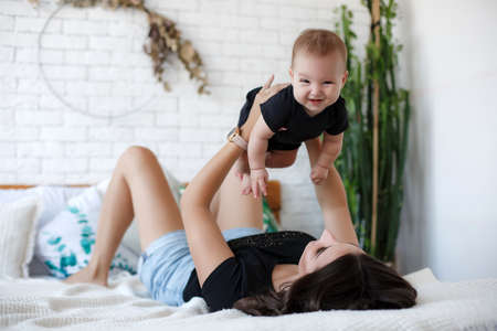 Mother and child on a white bed. Mom and baby boy in shorts playing in sunny bedroom. Parent and little kid relaxing at home.Family having fun together.の写真素材