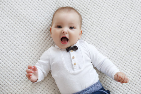 Adorable baby boy in white sunny bedroom plays alone lying on the bed.の写真素材