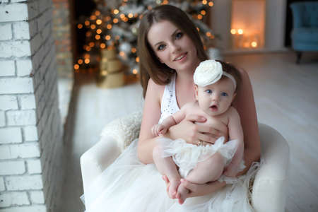 Happy mother holding a small child in her arms opposite the Christmas tree.New Year.christmas and family concept - portrait of happy young mother and cute little baby girl daughter near decorated christmas tree.の写真素材