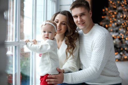 A happy family, father, mother and little daughter, spend time together on Christmas evening in a...