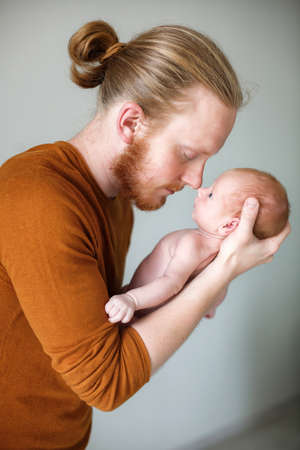 Closeup portrait of young bearded Caucasian father hugging and kissing newborn baby. Male man parent holding child. Authentic lifestyle touching tender moment. Single dad family life concept. Studio portrait of a happy father with a baby in his armsの写真素材