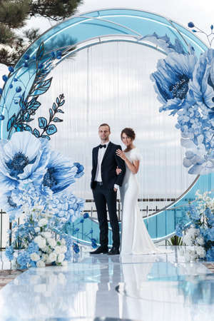 Wedding ceremony in an outdoor Banquet hall decorated with huge blue flowers. The bride and groom hold each other's hands. Banquet on the wedding day in a summer restaurant with beautiful decoration and design.の写真素材