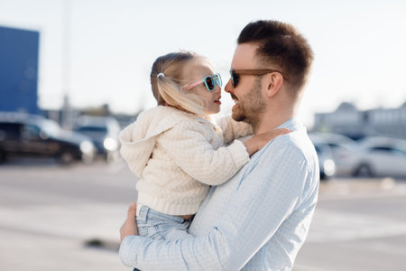 A happy father with a small daughter on his shoulders is walking in the parking lot