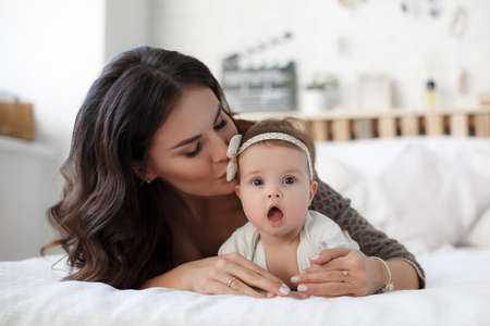Mother and child on a white bed. Mom and baby boy in shorts playing in sunny bedroom. Parent and little kid relaxing at home.Family having fun together. Bedding and textile for infant nursery. Happy lfamily. Mother playing with her baby in the bedroomの写真素材