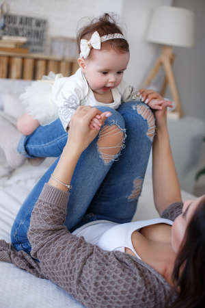 Mother and child on a white bed. Mom and baby boy in shorts playing in sunny bedroom. Parent and little kid relaxing at home.Family having fun together. Bedding and textile for infant nursery. Happy lfamily. Mother playing with her baby in the bedroomの写真素材
