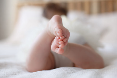 Adorable baby girl in white sunny bedroom plays alone lying on the bed.Charming beautiful lovely...