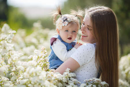 Portrait of a young mother and her little daughter in the park on a spring day. Beautiful woman with a little daughter in nature among flowering white bushes. Mom and daughter are resting together inの写真素材
