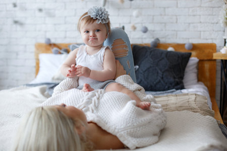 Mom and baby girl playing in sunny bedroom.Parent and little kid relaxing at home.Family having fun...