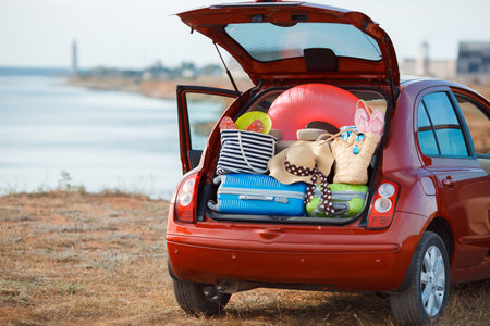A car with an open large trunk, loaded with things for the sea. Tourists on vacation by the ocean. Travel items in the car. Travel and outdoor activities on a deserted beach. Travel background.の写真素材