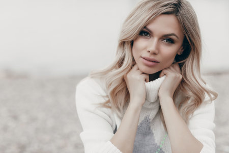 Young beautiful blonde caucasian woman walks alone enjoying the spring weather. Beautiful girl, outdoor portrait. Young attractive woman, spring outdoor portrait. Charming cheerful womanの写真素材
