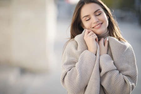 Young beautiful business woman with long hair and a beautiful smile in the spring city in a fashionable coat, walking along the street alone in the evening at sunset. Spring portrait of a happy womanの写真素材