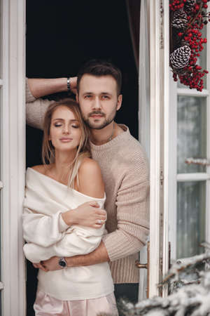 The guy and the girl hug, spending time together at the open door of the veranda, looking at the winter landscape.Happy couple in love spending time together on their honeymoon on their honeymoon tripの写真素材