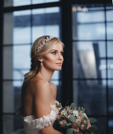 Pretty bride with wedding makeup, fashion jewelry. Beautiful woman posing in white wedding dress. Wedding portrait of happy bride. Bridal fashion model posing in interior. Gorgeous beauty, young brideの写真素材