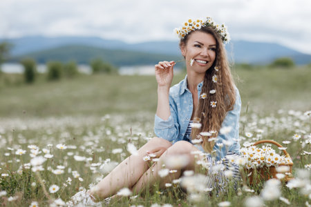Young, beautiful woman in a wreath of wild flowers, spends time alone outdoors among white meadow daisies. Beautiful girl outdoors with a bouquet of flowers in a field of white daisies, enjoying nature.の写真素材