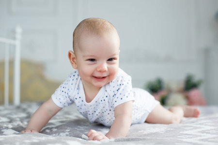 A charming boy in a white sunny bedroom plays alone, lying on the bed.A charming cute little boy...
