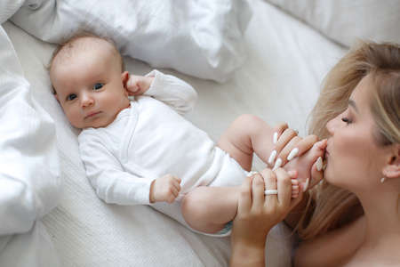 Newborn baby feet in mother hands. Close up of mother hand massaging foot newborn baby lying on comfortable white bed at home. Caucasian loving mom takes care of her infant son.の写真素材