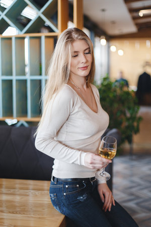 Young woman sitting alone at desk with glass of wine. Beautiful gorgeous girl drinking alcohol in a restaurant alone. Women's hands holding a large wine glass with red wine.の写真素材