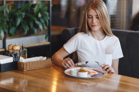 Young pretty woman with long hair dines with a glass of white wine in a restaurant. Inspired young woman enjoying champagne and salad in a restaurant on a summer weekend alone.の写真素材