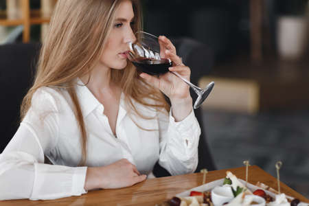 Young pretty woman with long hair dines with a glass of white wine in a restaurant. Inspired young woman enjoying champagne and salad in a restaurant on a summer weekend alone.の写真素材