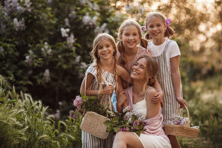 Cheerful girlfriends spend time outdoors in the park in spring among the fragrant blooming lilacs. A girls with lilac flowers in the spring at park Sisters walk together in a green park on a sunny dayの写真素材