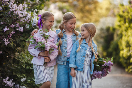 Cheerful girlfriends spend time outdoors in the park in spring among the fragrant blooming lilacs. A girls with lilac flowers in the spring at park Sisters walk together in a green park on a sunny dayの写真素材