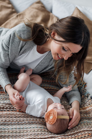 Mother and child on a white bed.Mom and baby boy in a white t-shirt playing in sunny bedroom. Parent...