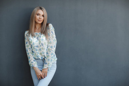 A beautiful young woman with long straight hair and brown eyes, a blonde with a pleasant smile, long black eyelashes dressed in a blue and white blouse, posing in the studio on a gray-blue backgroundの写真素材