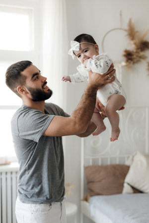 Portrait Of Happy Young Arab Dad Holding His Little Daughter On Hands. Portrait of happy middle eastern father and newborn daughter having fun at home in bedroom. Father Daughter Love.の写真素材