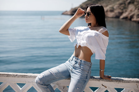 Summer portrait of a young beautiful brunette woman outdoors spending time alone posing by the sea...