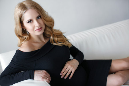 Partial nudity. A young pregnant woman with long, blond, curly hair is talking to an unborn child, the expectant mother is stroking her belly. The last months of pregnancy, studioの写真素材