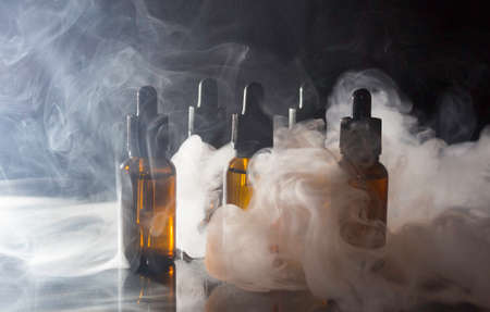 Glass bottles with pipettes and VAPE liquid. Thick vapor from Smoking an electronic cigarette.の写真素材