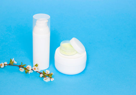 Face cream on a blue background, side view. Twig with flowers in the foreground. Caring for the...