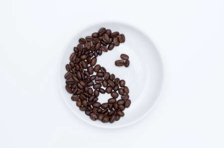 Yin Yang sign of coffee beans on a white saucer top view, white background. Concept of the pleasure of drinking coffee.の写真素材