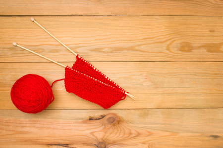 Red ball of yarn with spokes on a wooden background, free space for text.