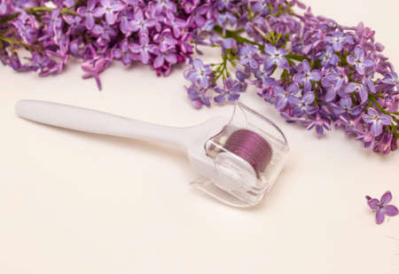 Mesoroller and lilac flowers on a white background. Concept of skin care, anti-wrinkle, Spa.の写真素材