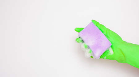 Hand in an green rubber glove with an purple sponge and foam on a white background. Washing dishes, cleaning, home cleaning.の写真素材