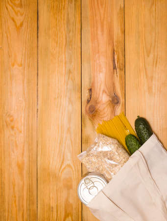 Food donations in a cloth bag on a wooden background, top view with copy space. Vertical photo.の写真素材