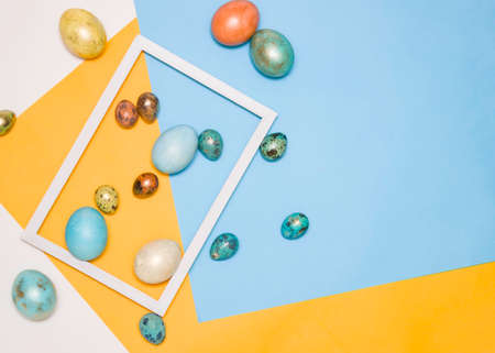 Colored Easter eggs in a wooden white frame and next to it on a white, yellow and blue background. Free space for text. Happy Easter!の写真素材