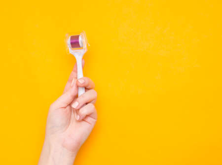 Mezoroller, dermaroller, mesotherapy skin tool in a woman's hand on a yellow background. Copy space.の写真素材