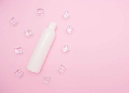 White plastic bottle for shampoo or other cosmetics. Ice cubes around, pink background, free space for text, top view.の写真素材