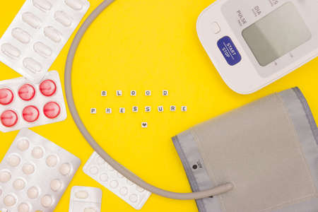 The concept of health, cardiology, blood pressure. BLOOD PRESSURE words on the dice. Blood pressure monitor, tablets and tissue heart on a bright yellow background. Top view, free space for textの写真素材